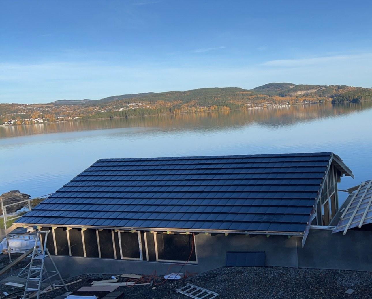 A new dark roof on a house above a lake, with hills across the water